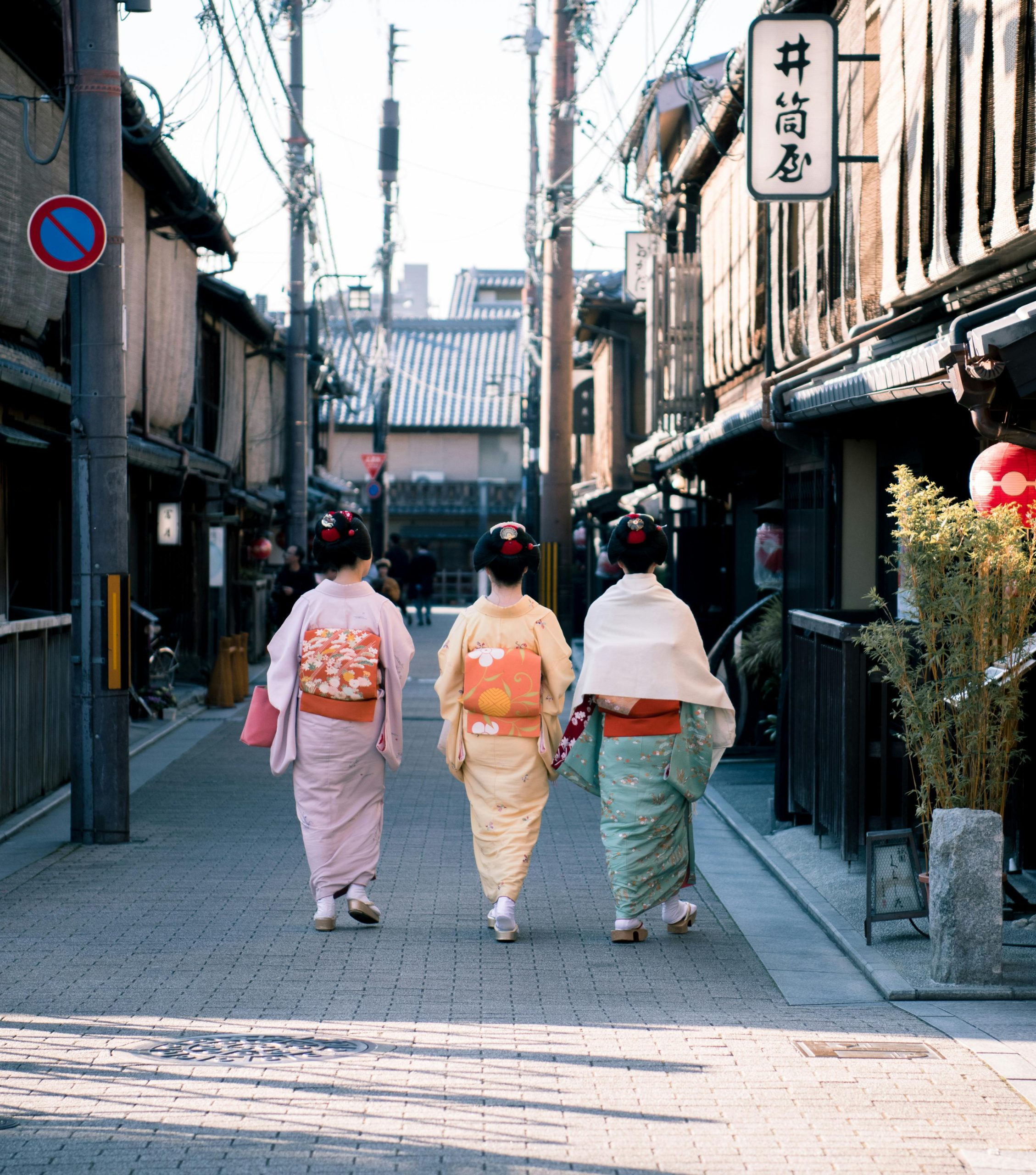 Three women wearing traditional kimonos walk down a historic street in Kyoto, Japan, capturing cultural essence.