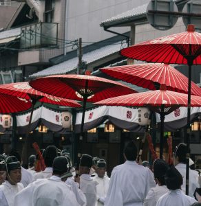 Cultural street procession in Kyoto, Japan, featuring traditional attire and red umbrellas.